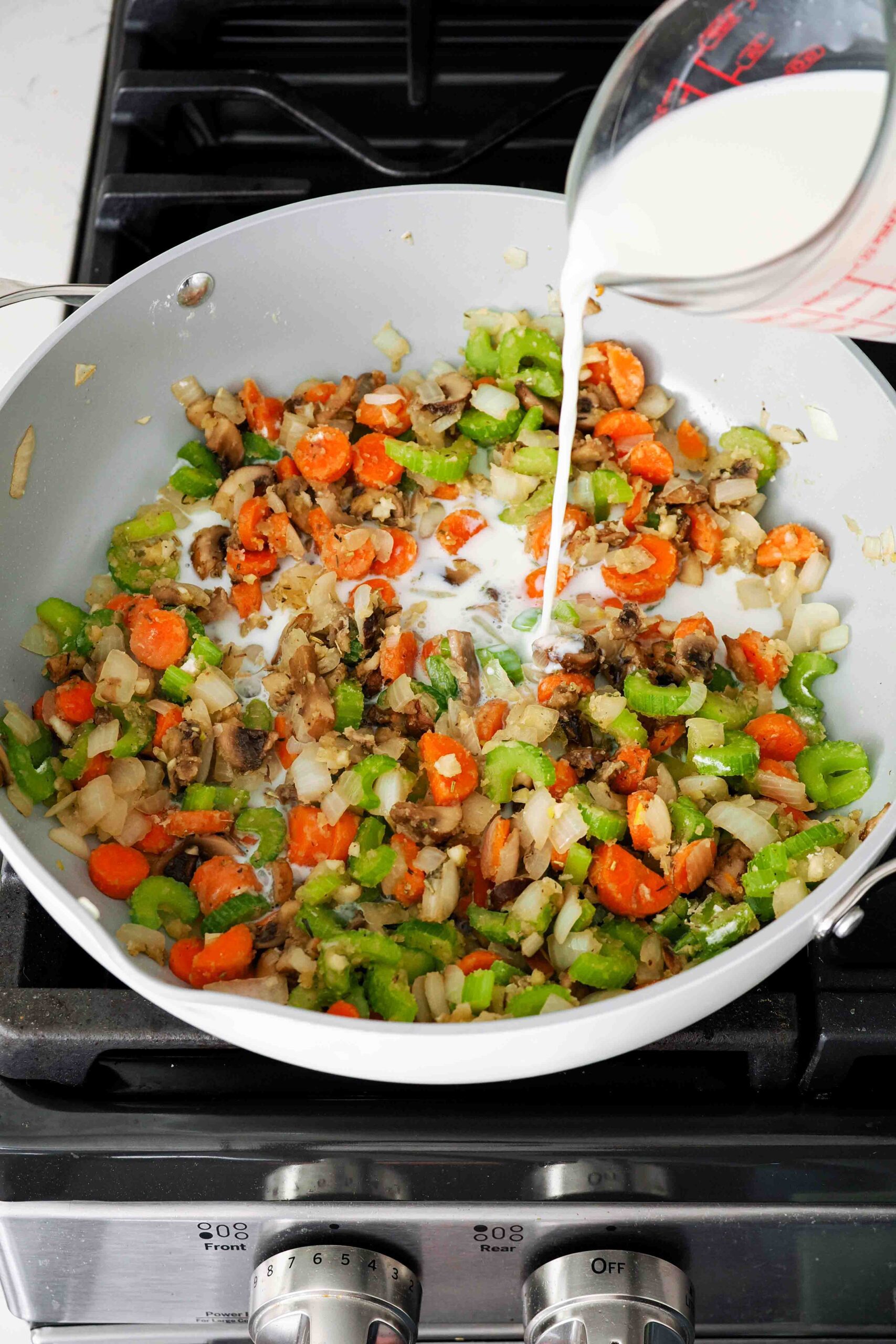 Milk is added to a pan full of sautéed vegetables with flour to create a sauce.