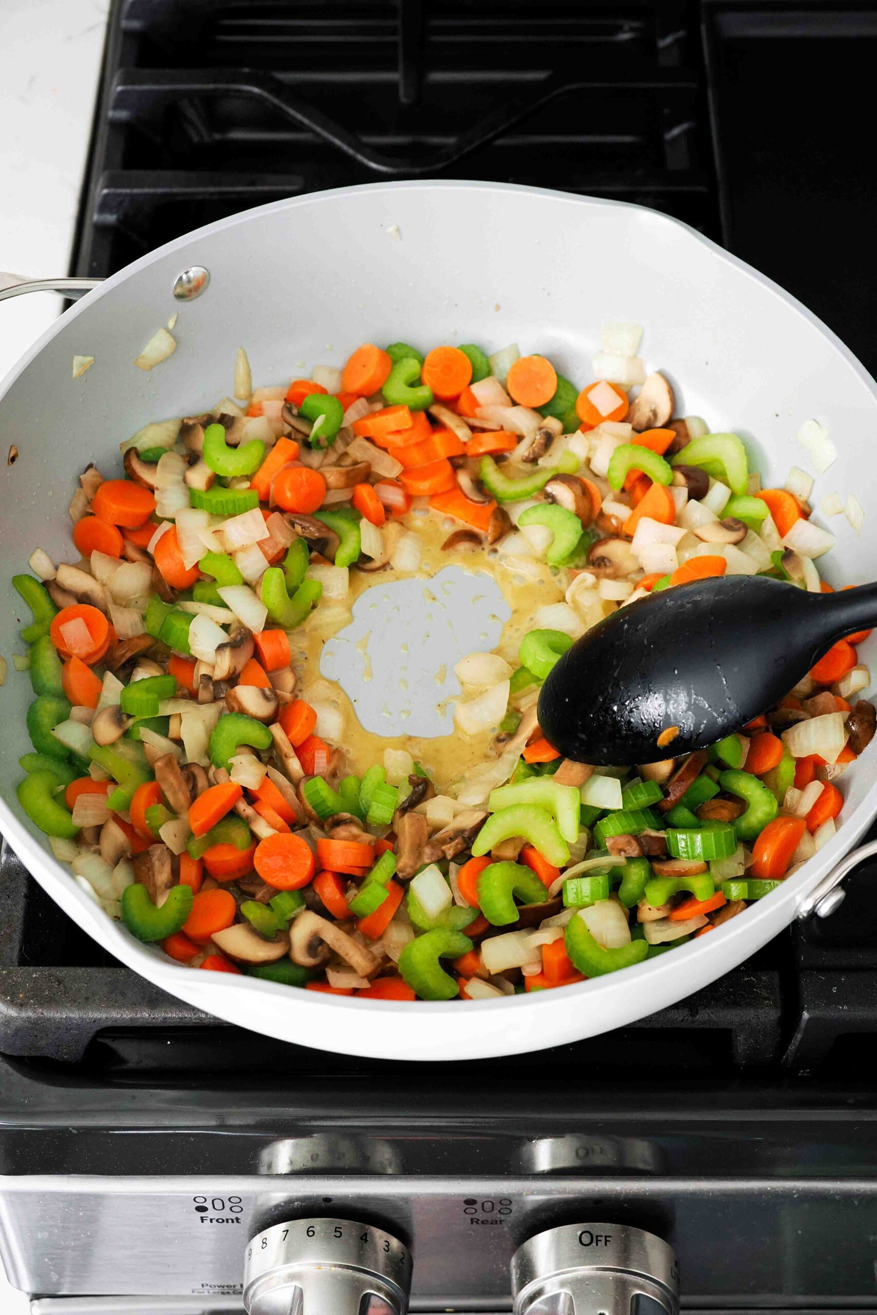 A spoon clears the center of a large pan with vegetables, and liquid seeps in.