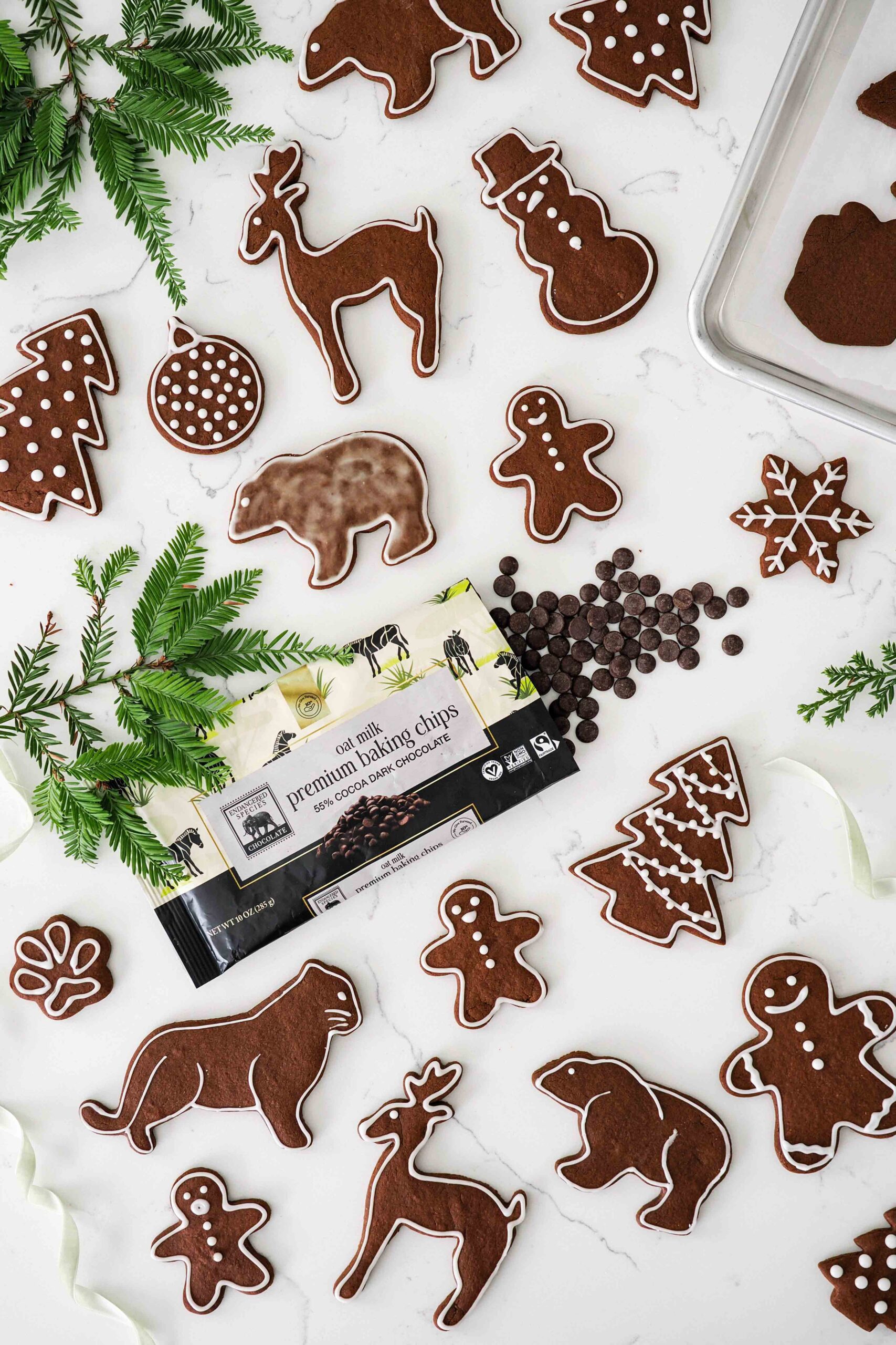 An overhead view of chocolate gingerbread cookies on a quartz counter with a bag of Endangered Species Chocolate baking chips and pine branches.