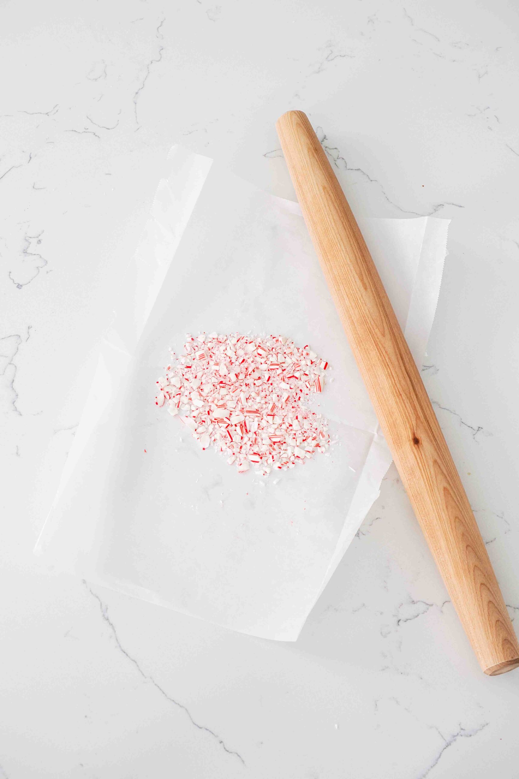 Crushed candy canes on parchment paper near a rolling pin.