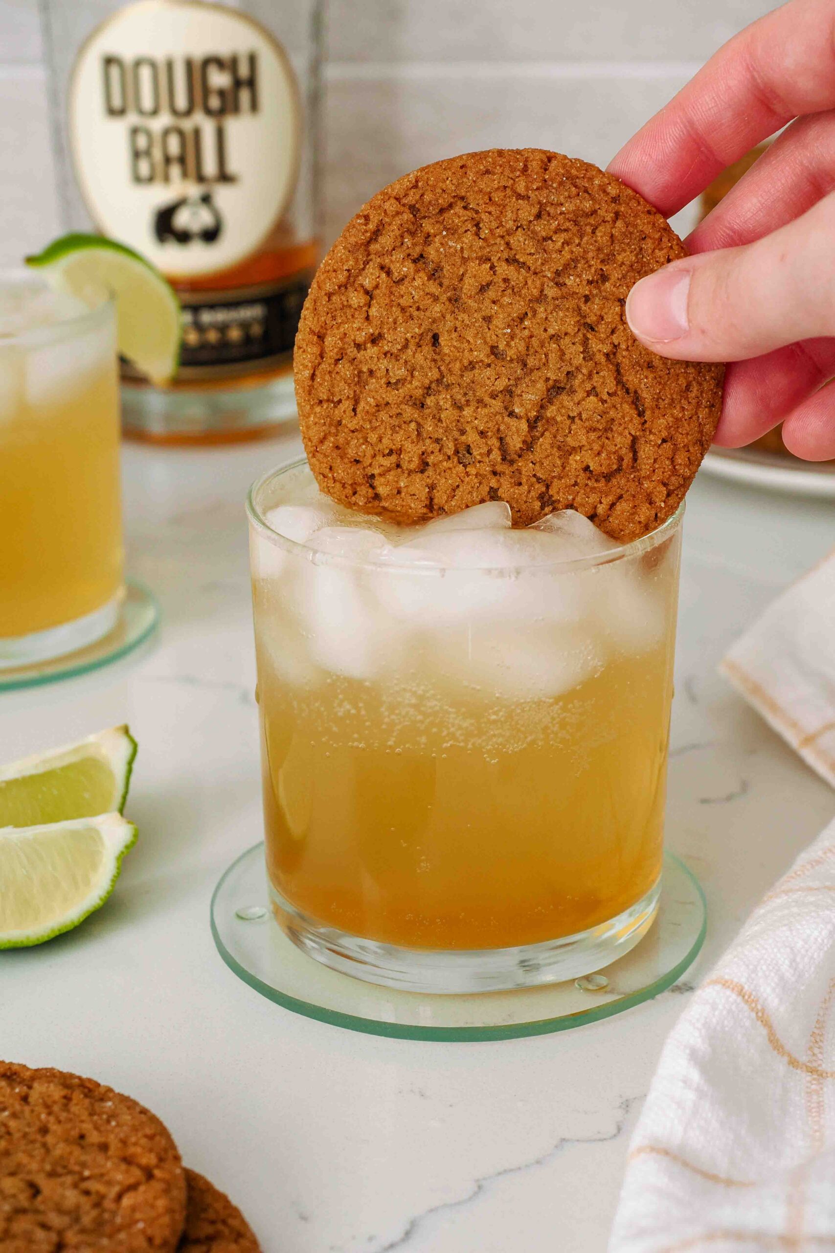 A hand dunks a gingersnap cookie into a lowball glass with a whiskey gingersnap cocktail.