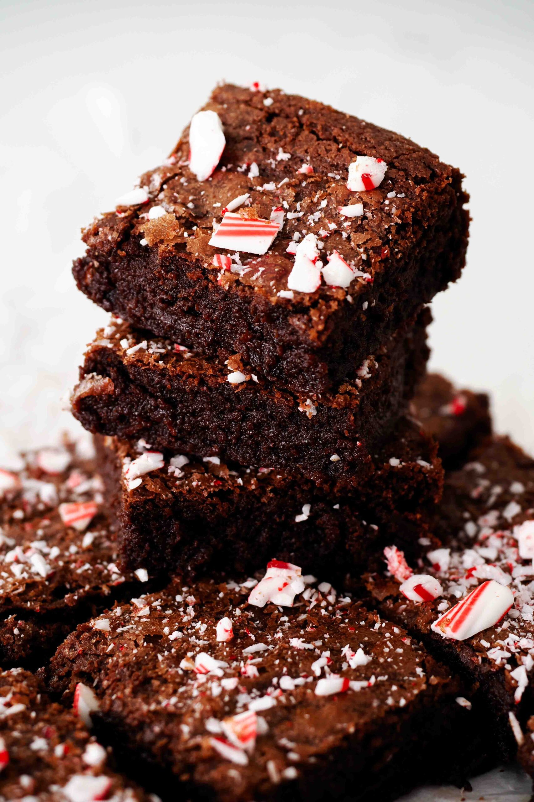 A stack of three peppermint brownies on top of a pan of brownies.