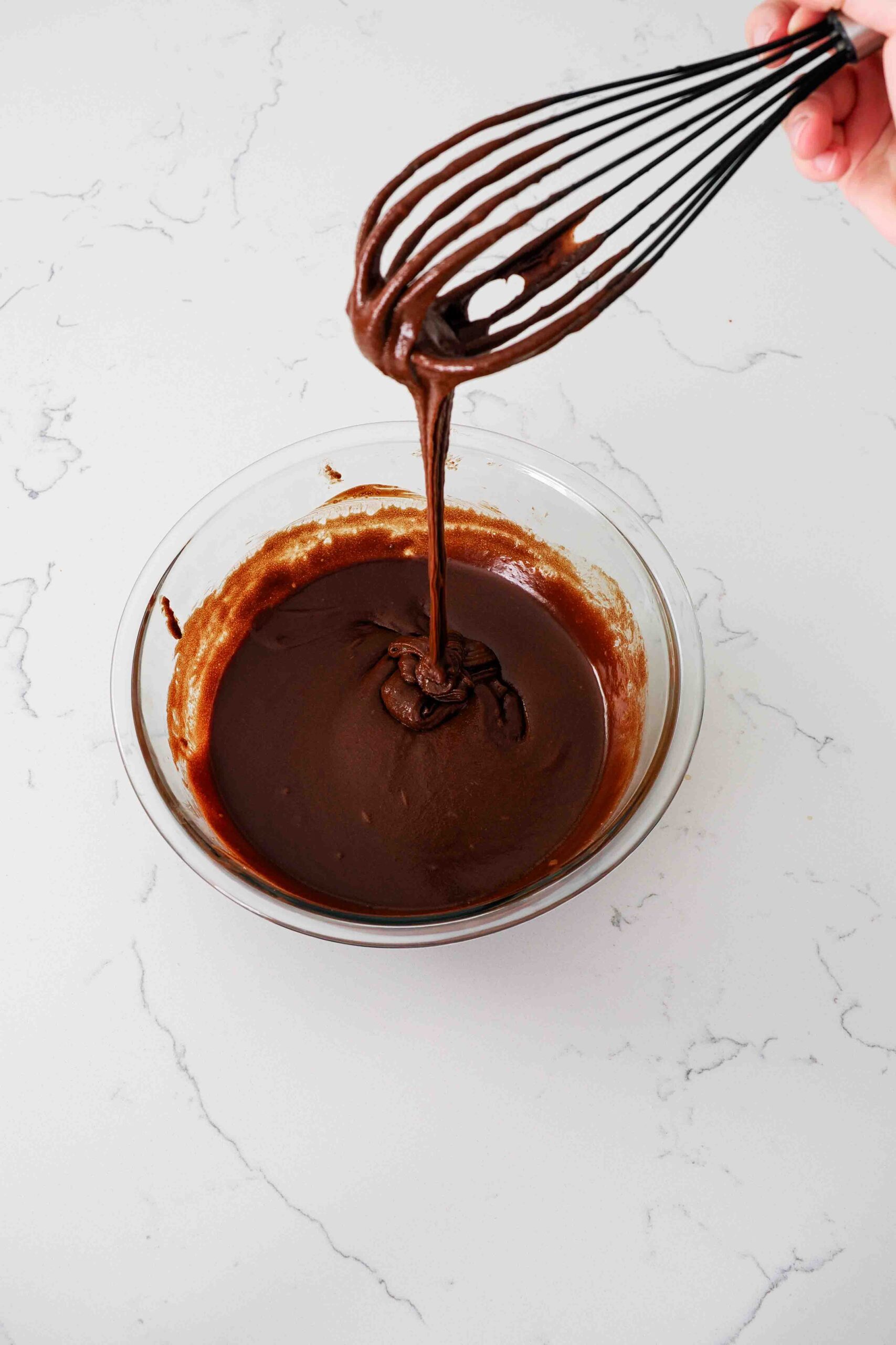 A whisk holds up brownie batter in the ribbon stage.