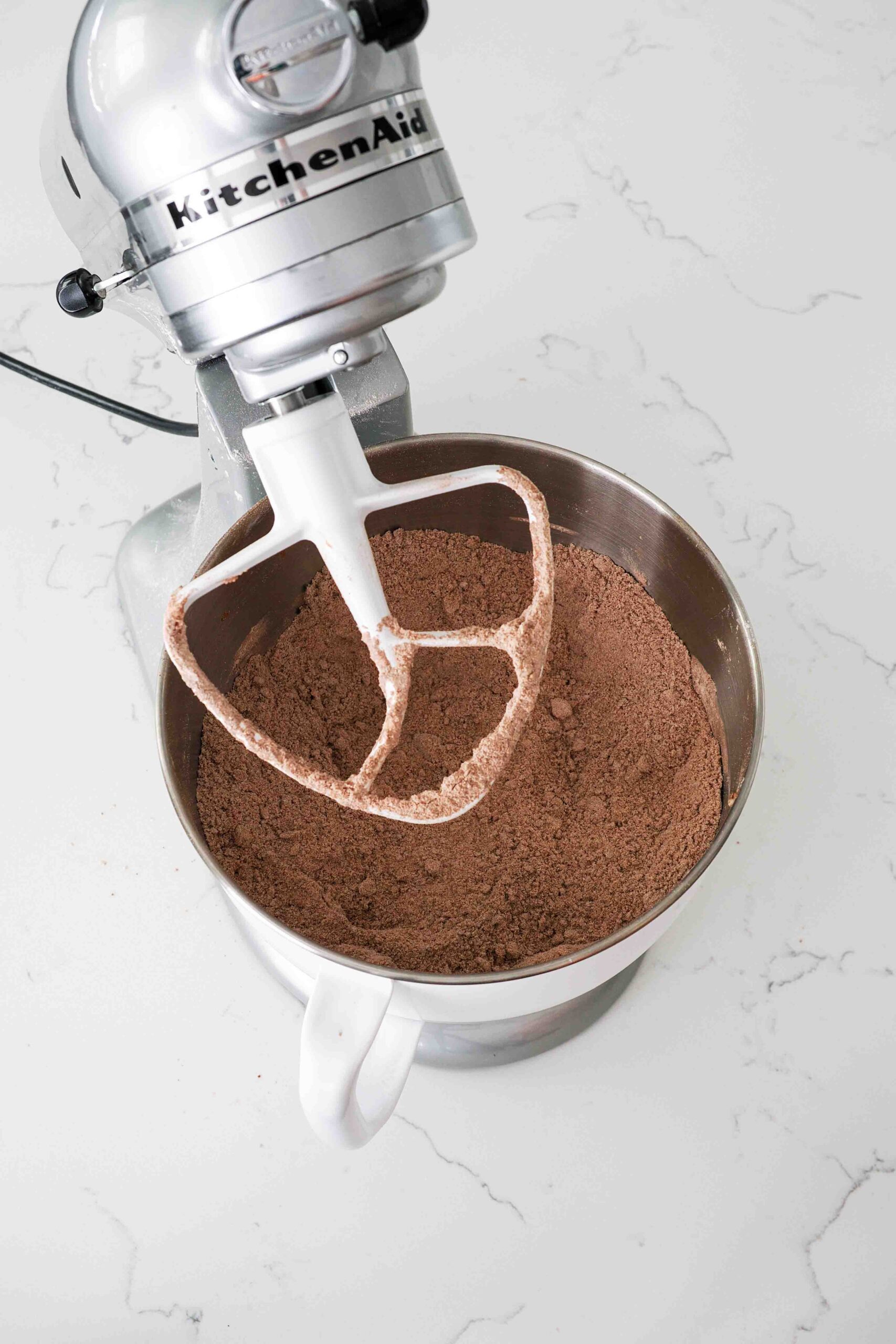 Dark and sandy-looking gingerbread cookie dough in a stand mixer bowl.
