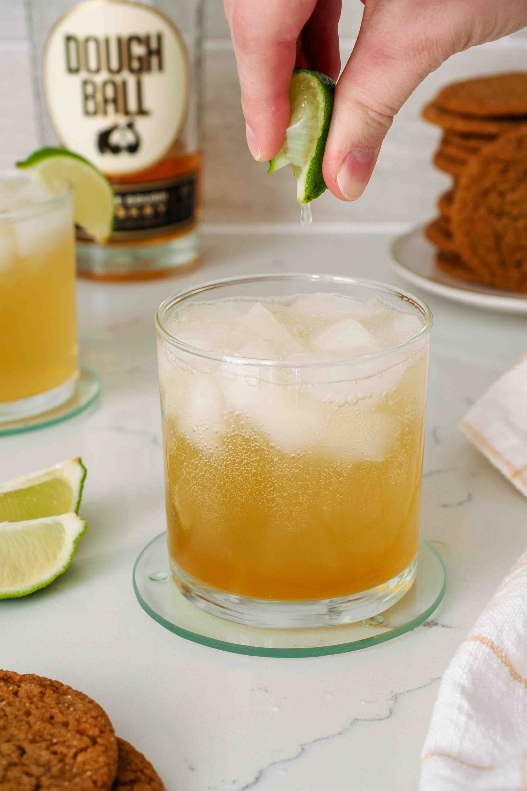 A hand squeezes lime juice over a whiskey gingersnap.