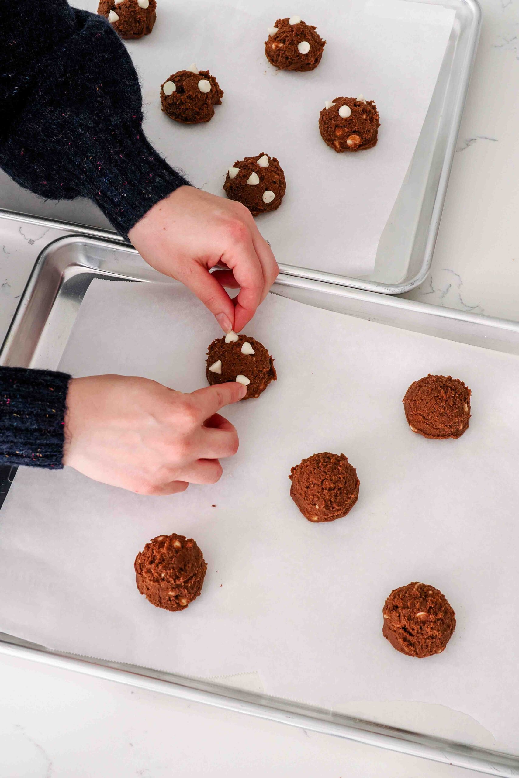 Two hands add peppermint chips to the outside of the chocolate cookie dough balls.