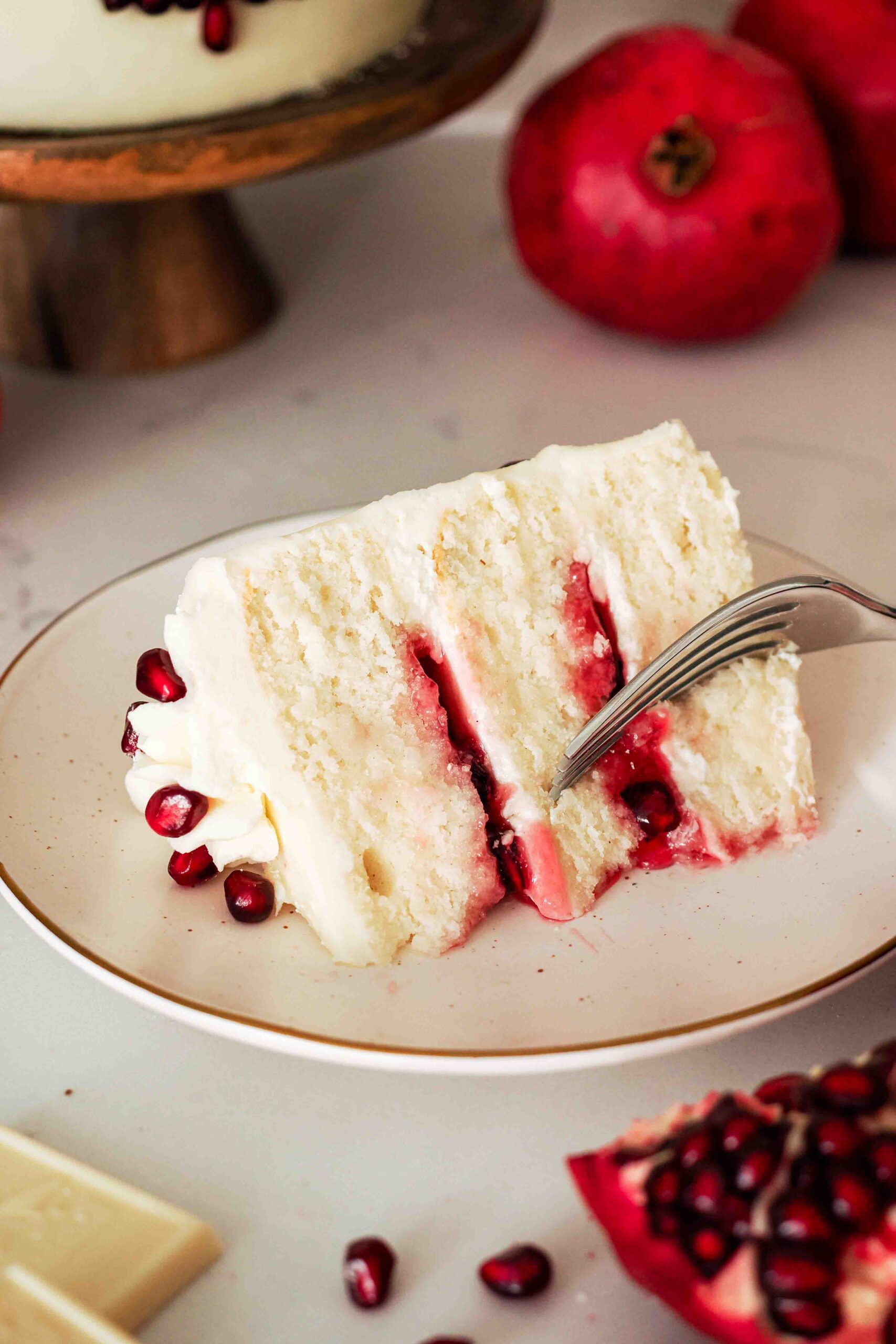 A slice of white chocolate pomegranate cake on its side and a fork taking a bite out of it.