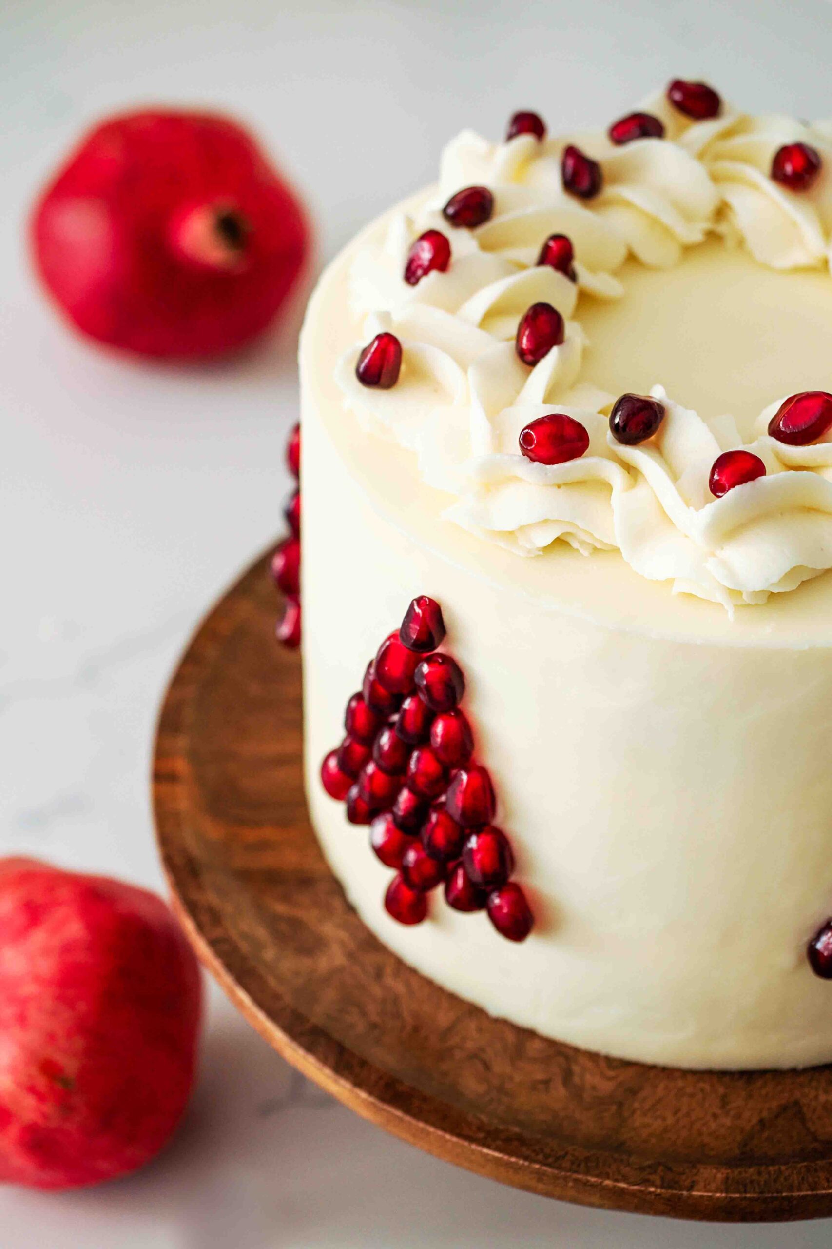 A white layer cake decorated with pomegranate seeds in the shape of a Christmas tree.