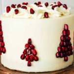 White chocolate pomegranate layer cake has a Christmas tree made out of pomegranate arils on the side.