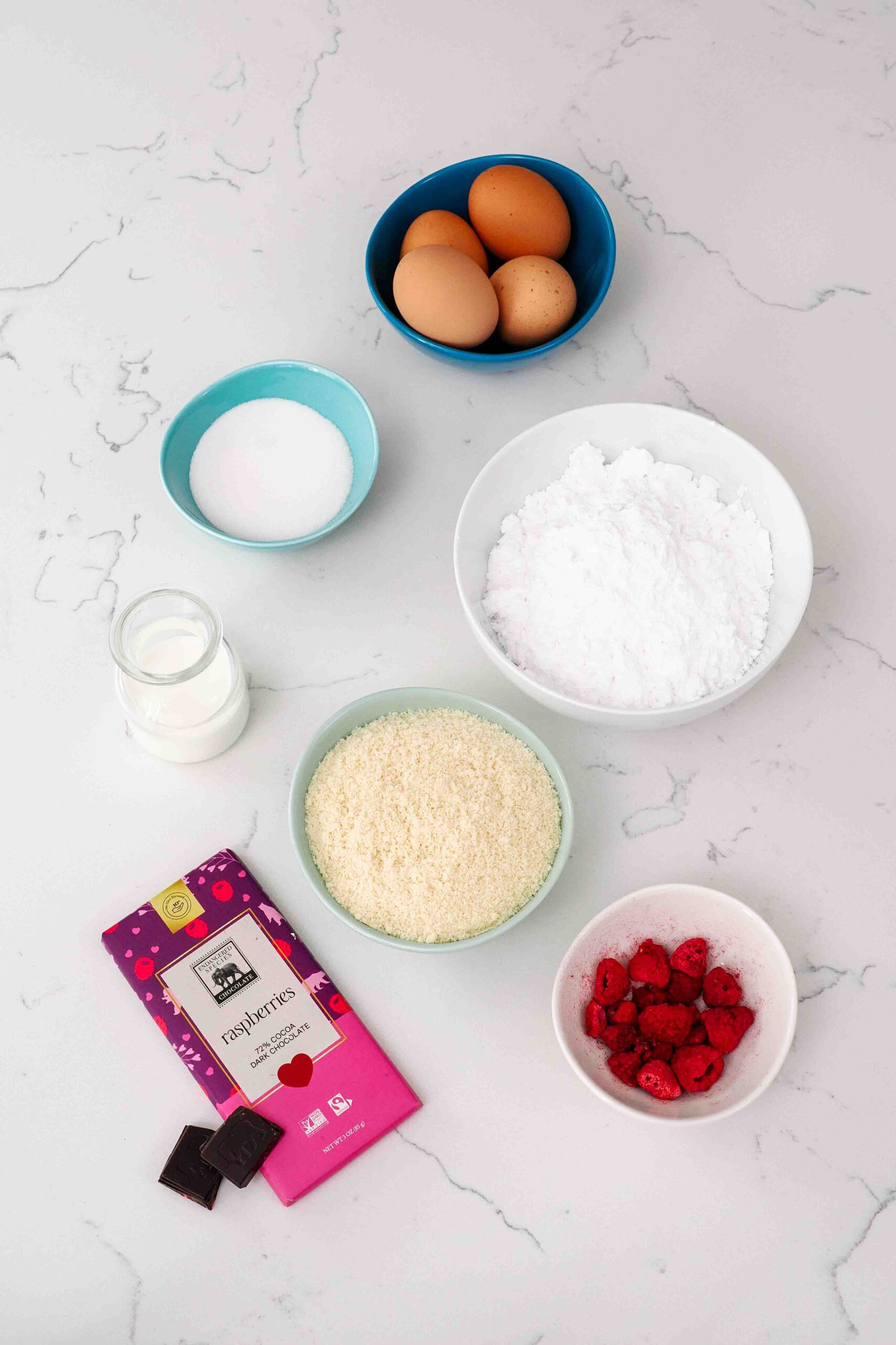 Ingredients for chocolate raspberry macarons on a quartz countertop.