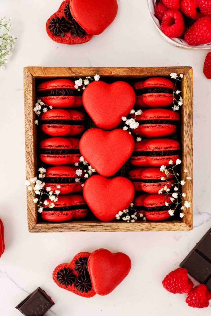 A wooden box is filled with red, heart-shaped macarons and baby's breath flowers.