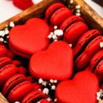 A wooden box is filled with red, heart-shaped macarons and decorated with baby's breath flowers.