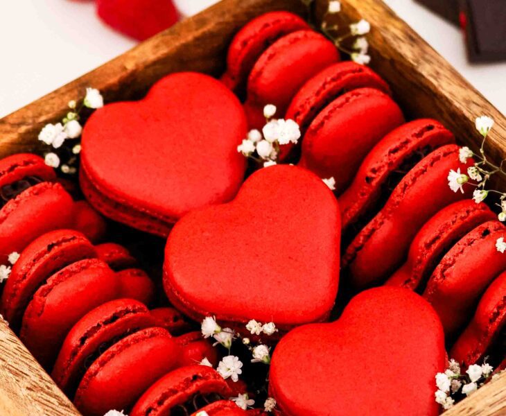 A wooden box is filled with red, heart-shaped macarons and decorated with baby's breath flowers.