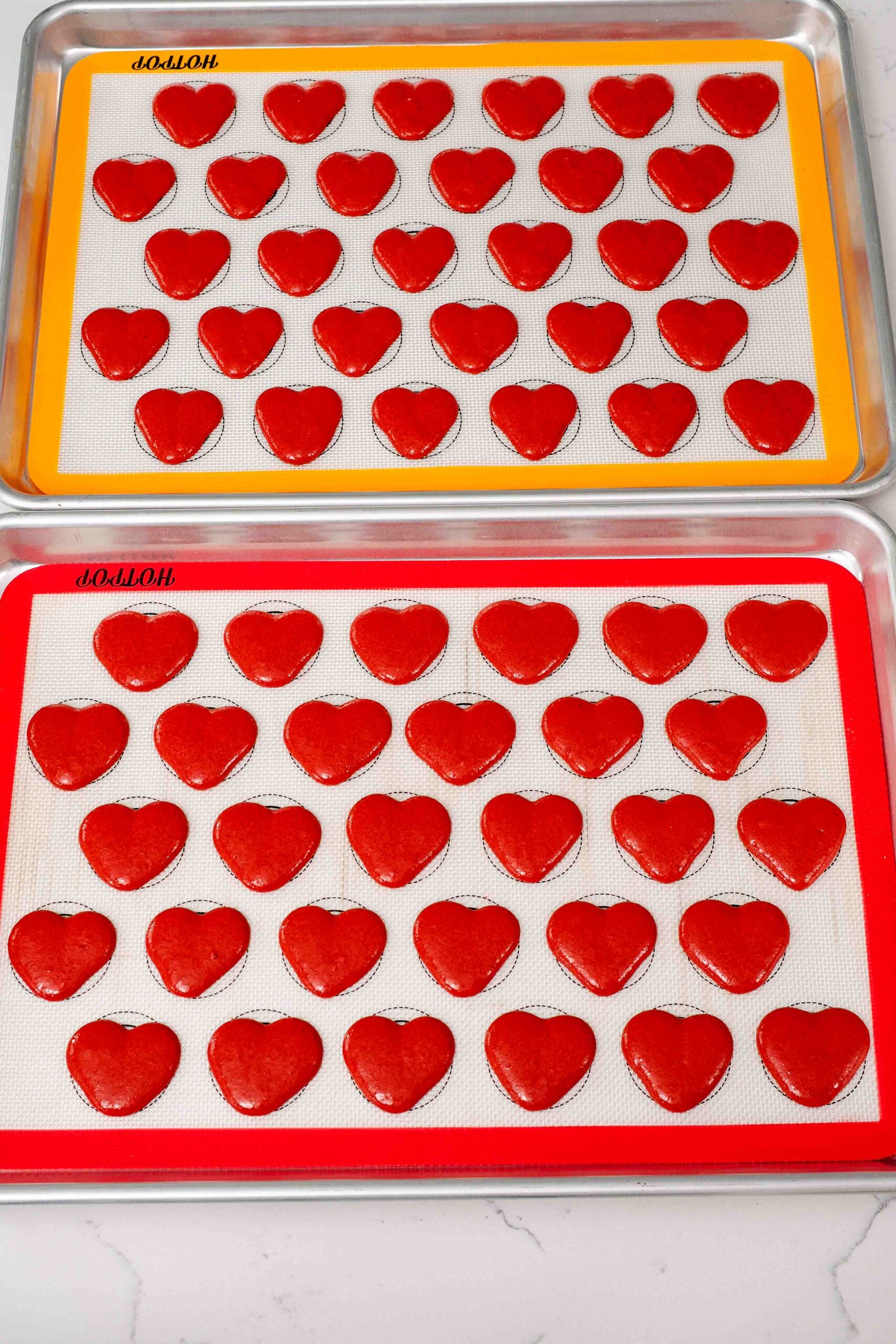 Freshly piped heart macarons on silicone macaron mats.