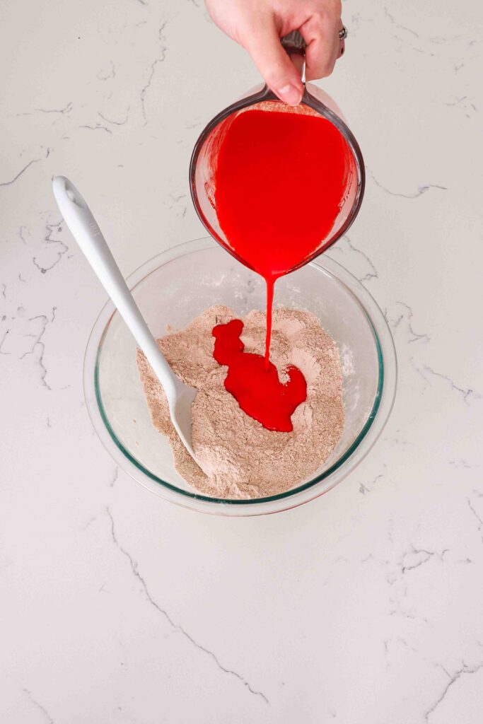 The liquid red velvet ingredients are poured into a glass bowl with the dry ingredients.