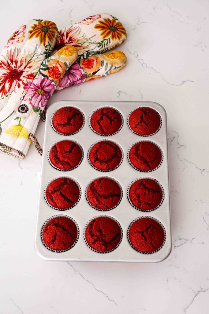 Fully baked red velvet cupcakes on a quartz counter.