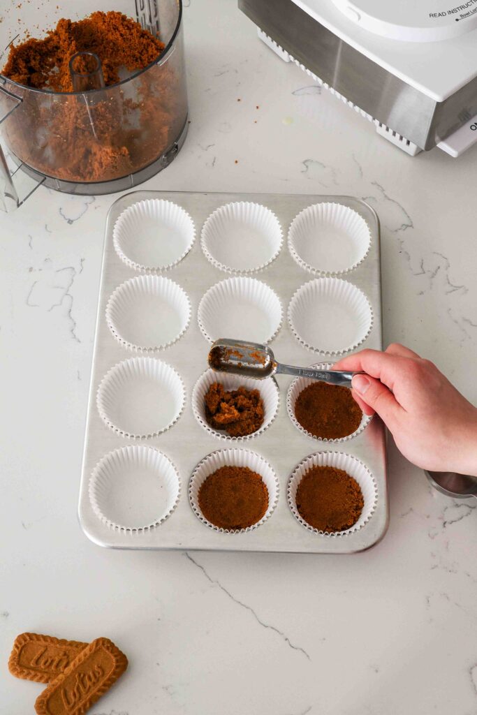 A hand adds cookie crumbs to paper liners in a muffin pan.