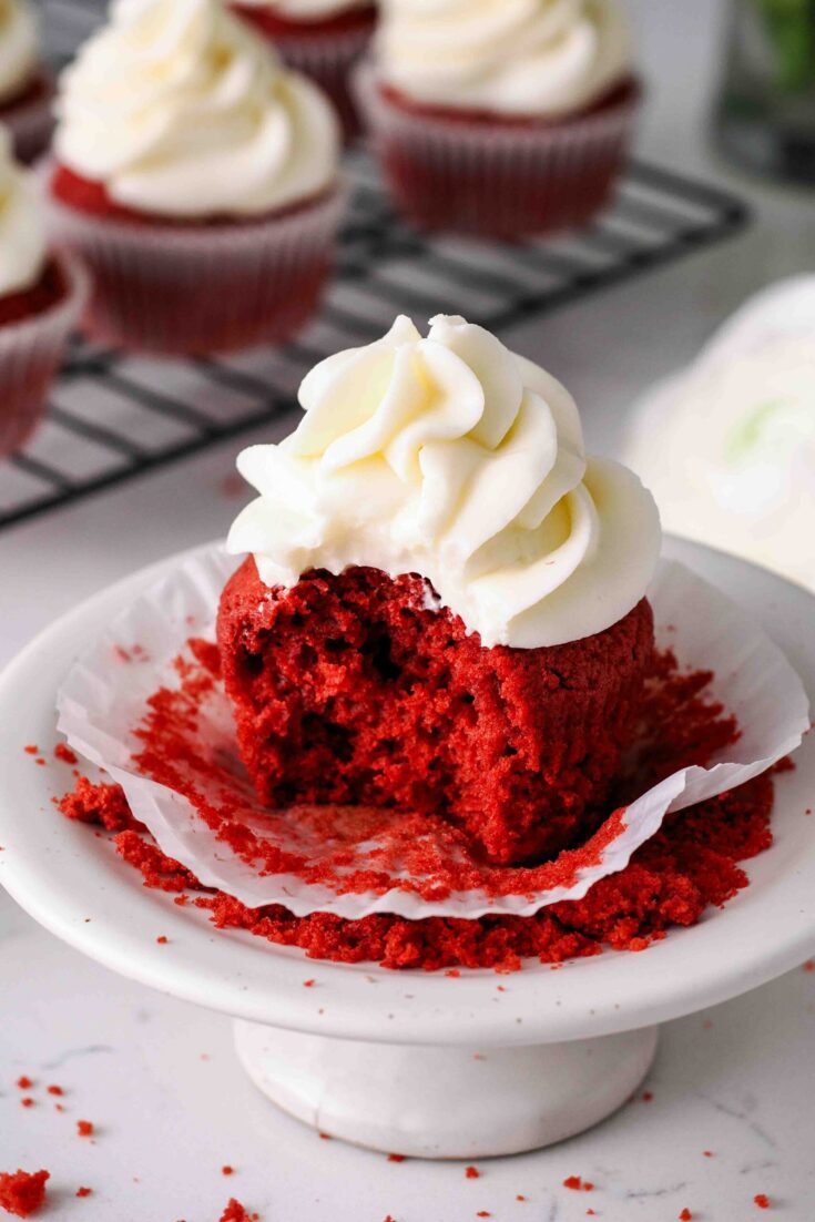 A bite is missing from a red velvet cupcake with a cream cheese frosting swirl.