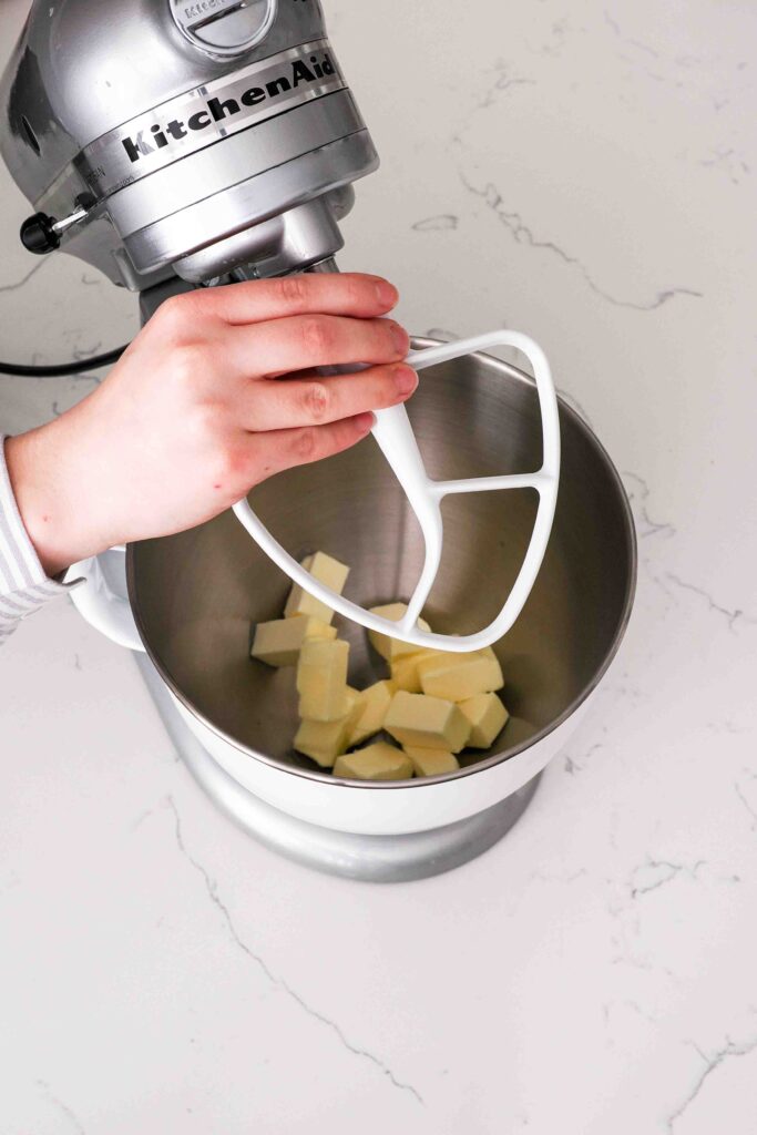 Butter sits in the bowl of a stand mixer fitted with a beater attachment.