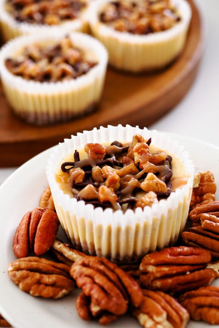 A closeup of a mini turtle cheesecake in a paper muffin liner on top of pecans.