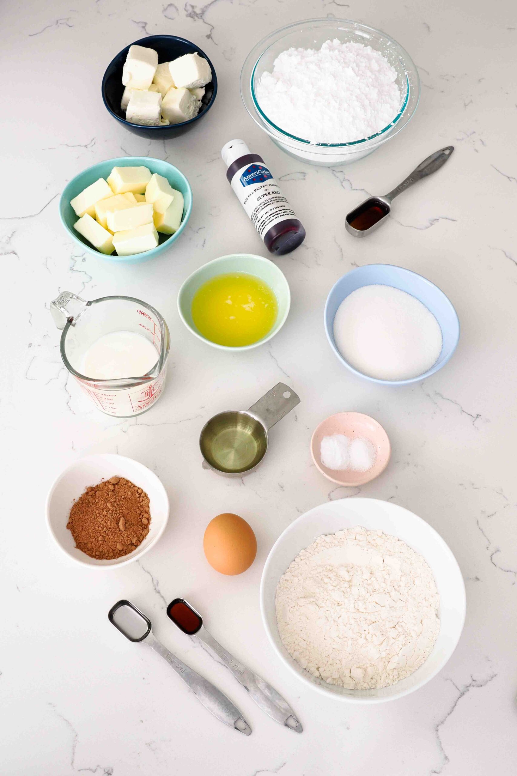Ingredients for red velvet cupcakes and cream cheese frosting on a quartz counter.