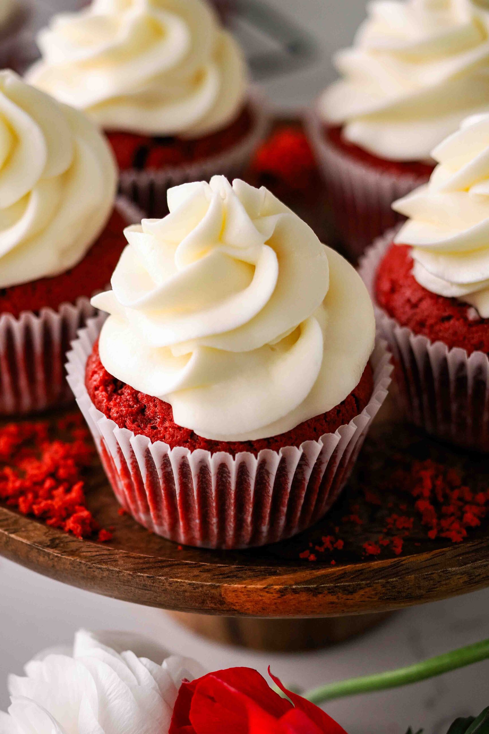Closeup of a red velvet cupcake with a cream cheese frosting swirl on a wooden platter.