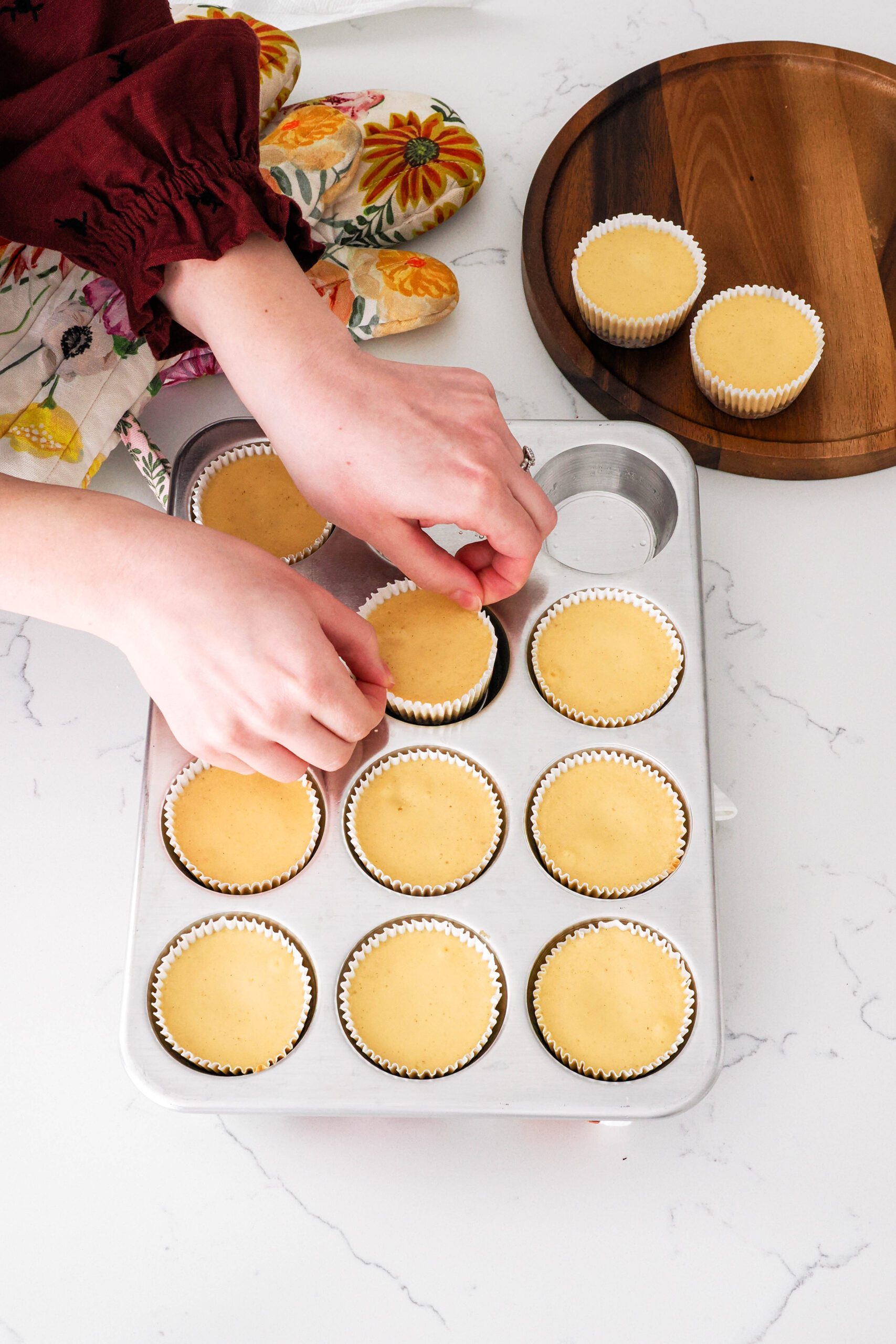 Two hands pinch the edges of the paper liner on a mini cheesecake to remove it from a muffin pan.