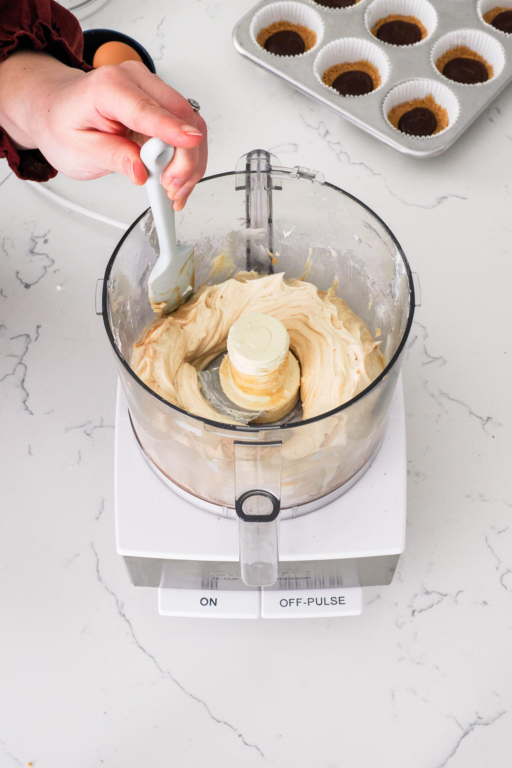 A spatula scrapes down the sides of a food processor bowl with caramel cheesecake.