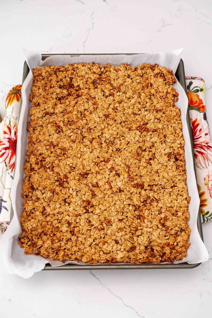 A pan of fully baked honey pecan granola cools on floral hot pads.