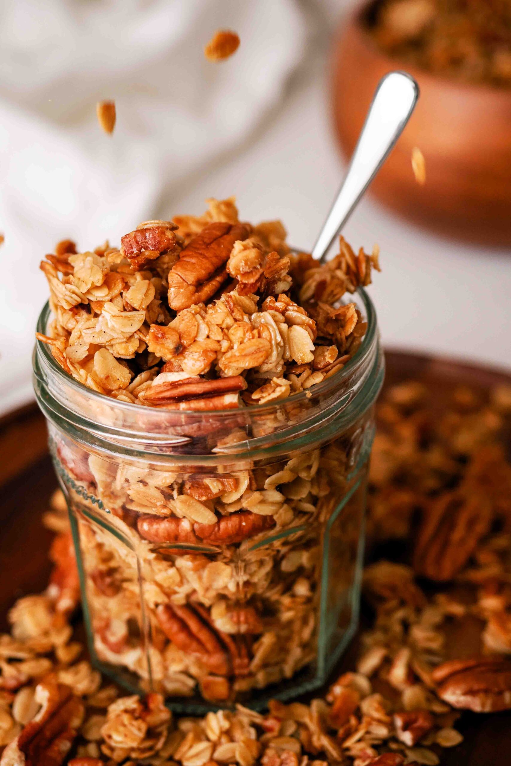 Clusters of honey pecan granola are dropped into a glass jar.