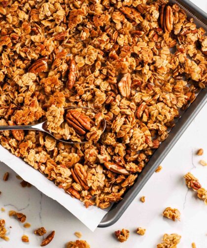 An overhead image of honey pecan granola clusters in a parchment-lined baking sheet.
