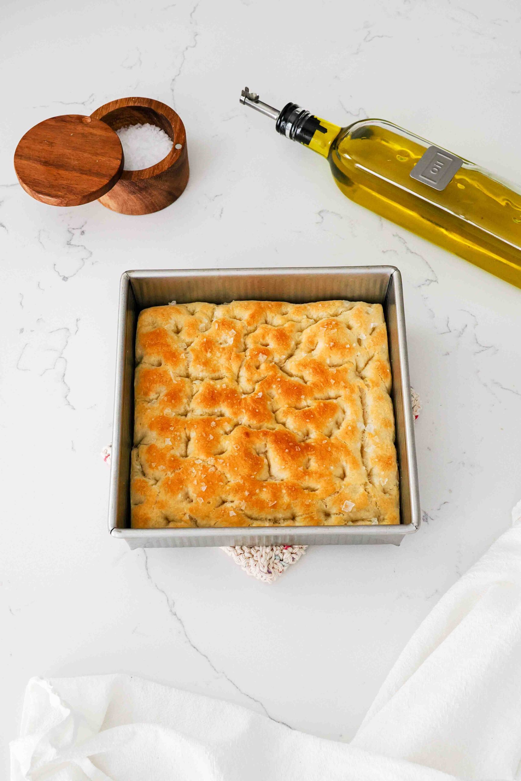 A golden brown loaf of focaccia bread in a square pan on a quartz countertop.