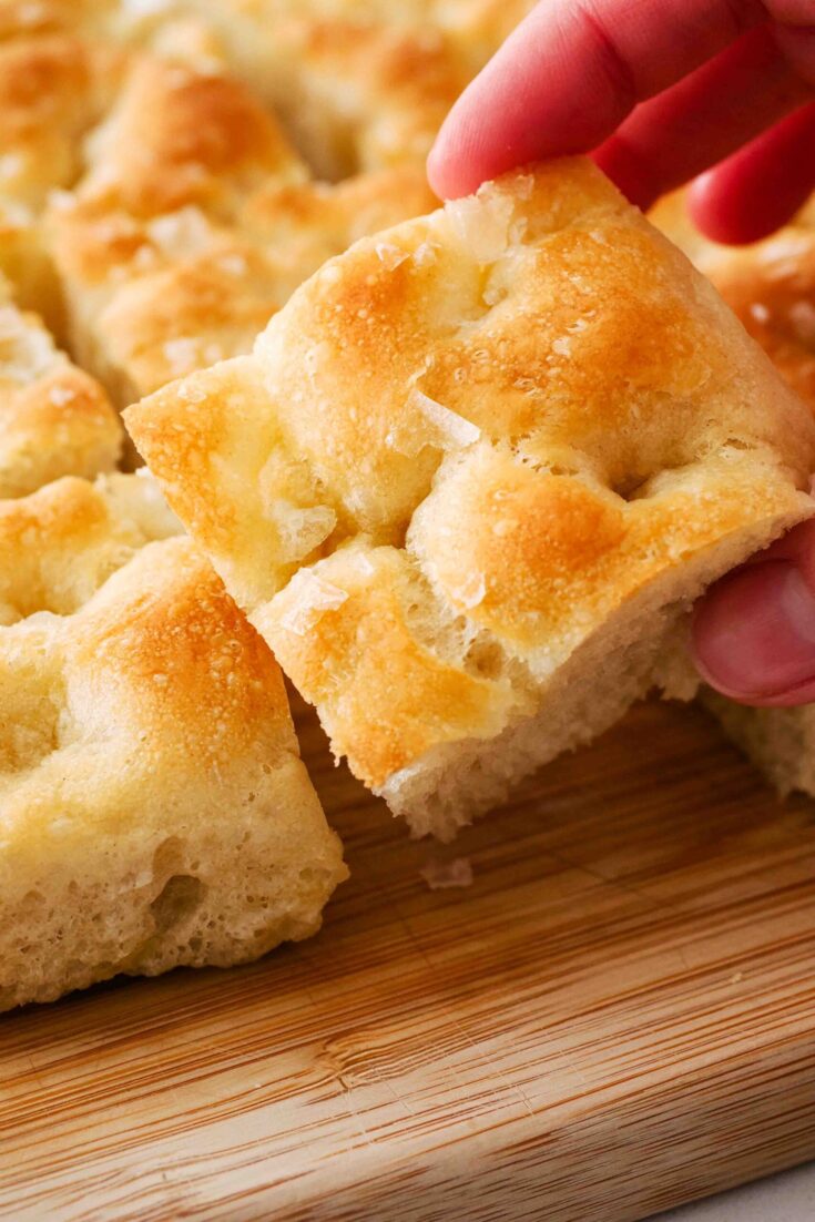 A hand picks up a golden brown square of focaccia bread.