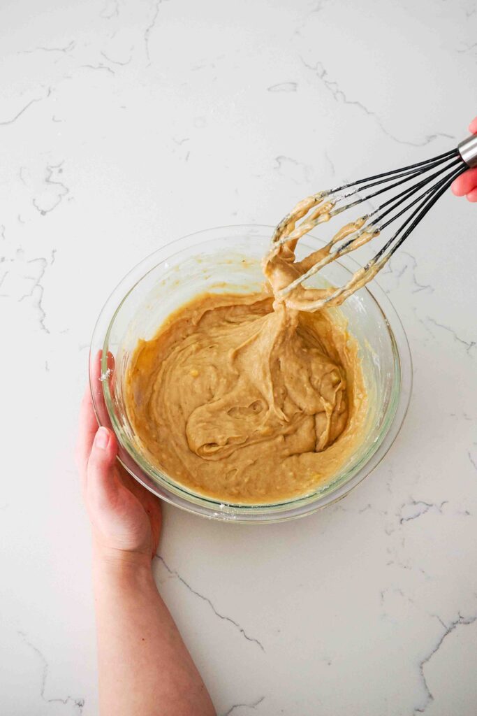 A glass mixing bowl with cinnamon banana bread batter being whisked.