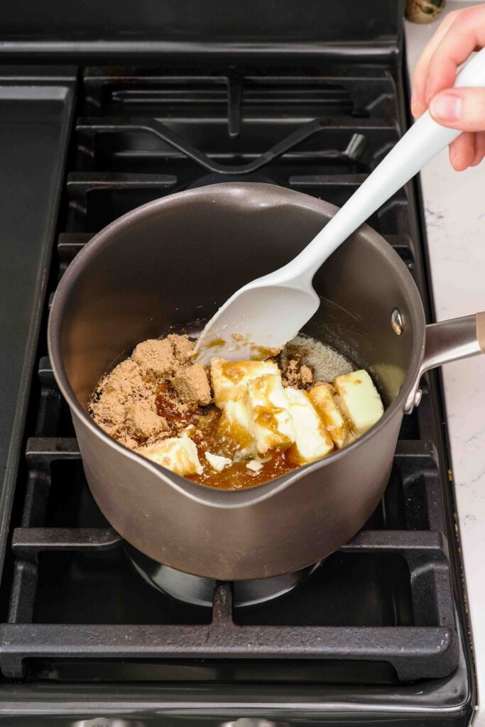 A spatula stirs brown sugar, butter, honey, and salt together in a pot.