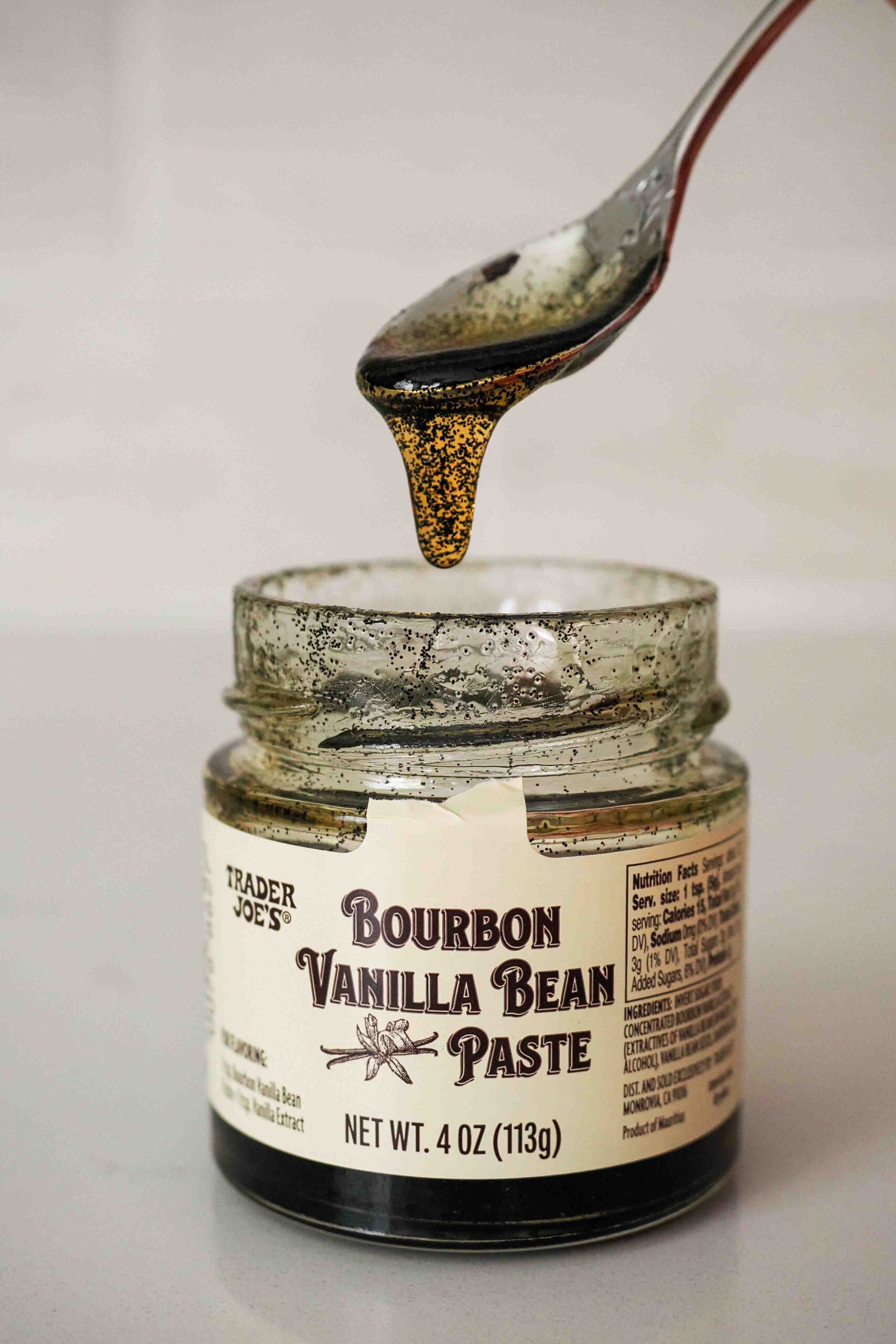 Trader Joe's Bourbon vanilla bean paste drips off a spoon back into its jar.