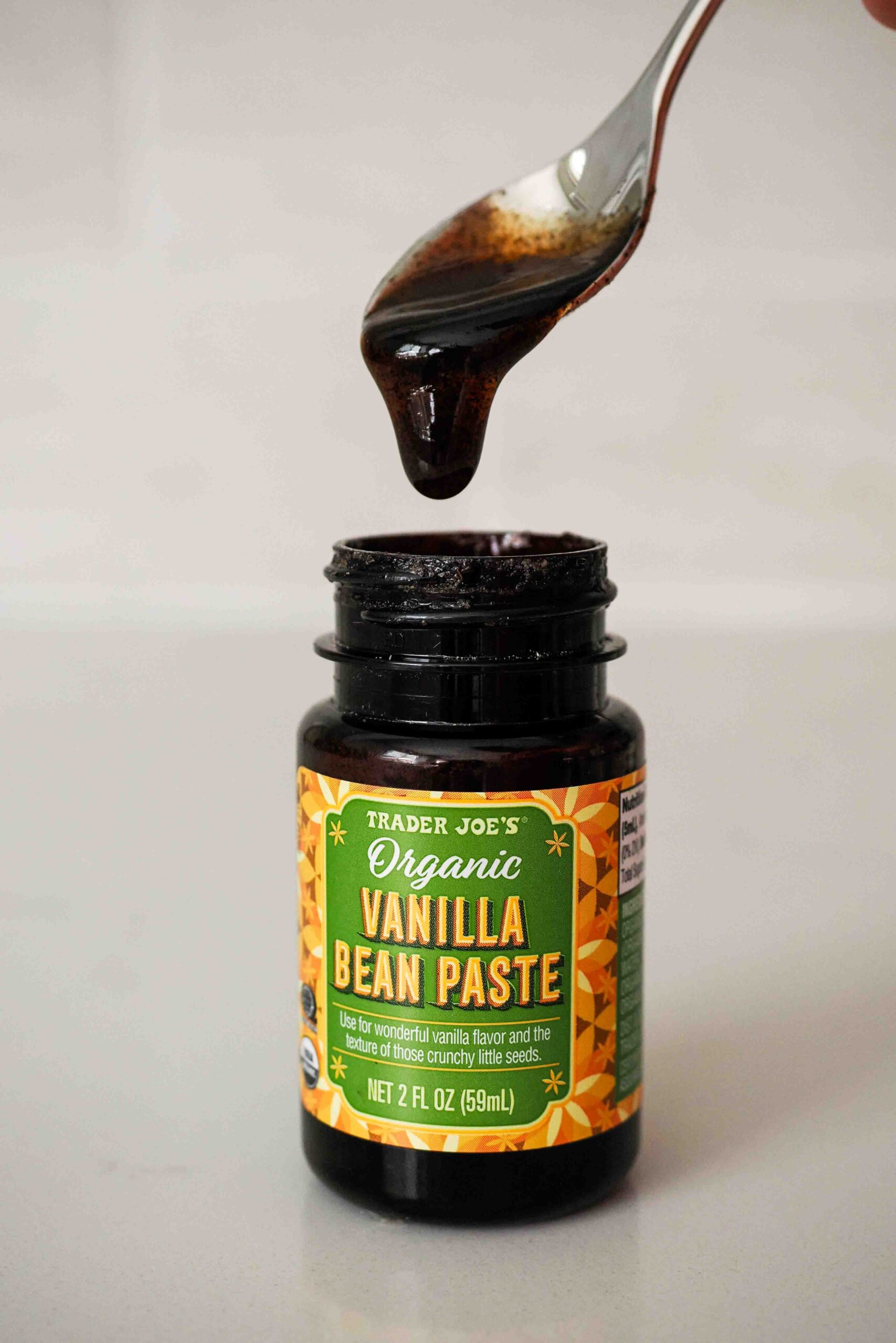 Trader Joe's organic vanilla bean paste drips off a spoon into its container.