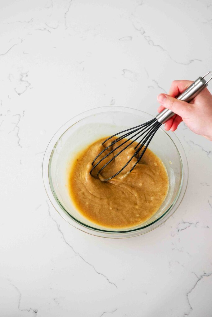 A hand whisks together the wet ingredients for cinnamon banana bread.