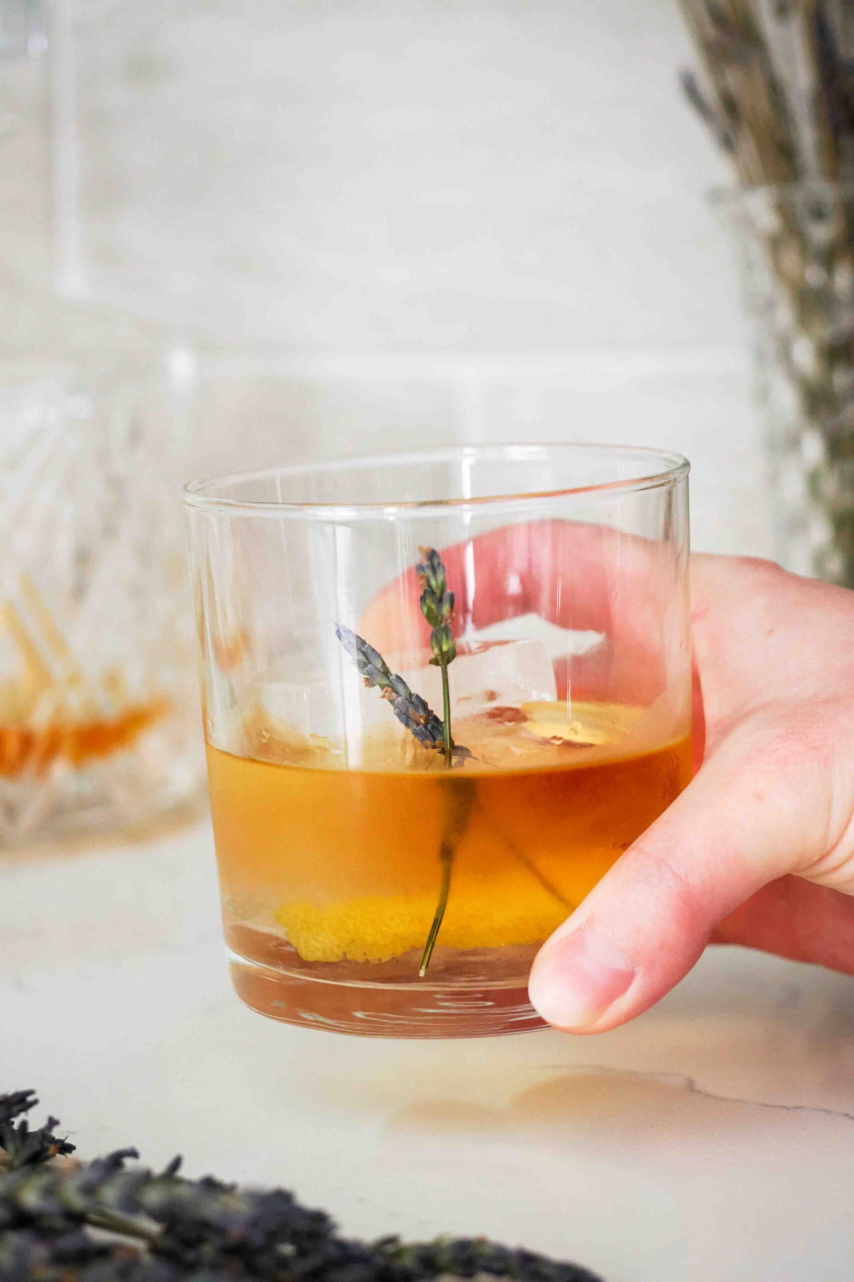 A hand picks up a rocks glass filled with a lavender old fashioned.