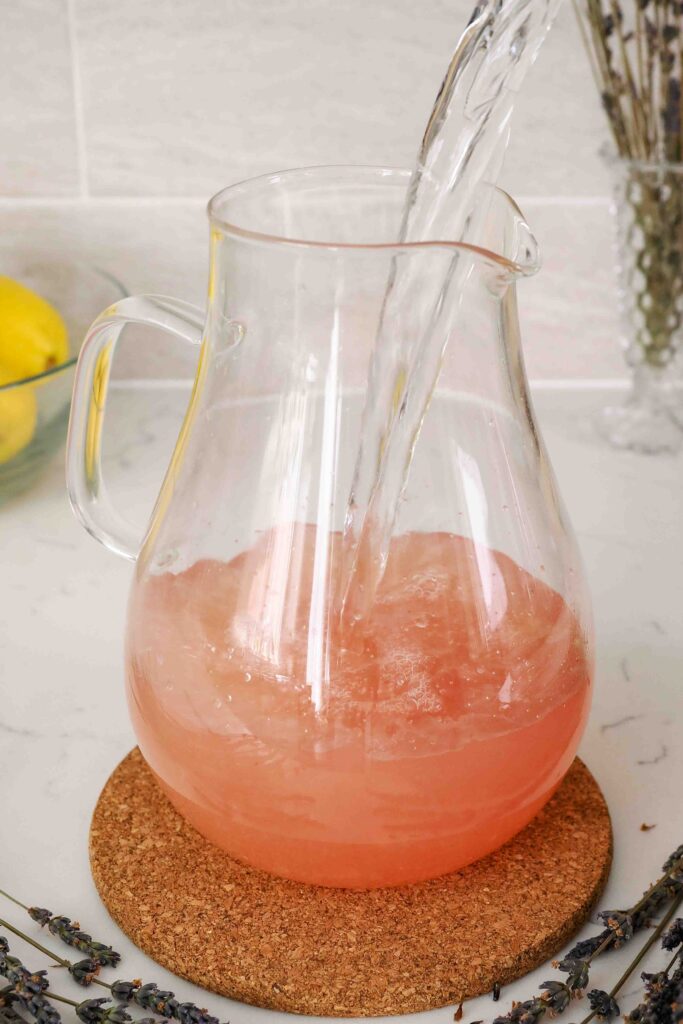 Water is added to a pitcher with bright pink simple syrup.