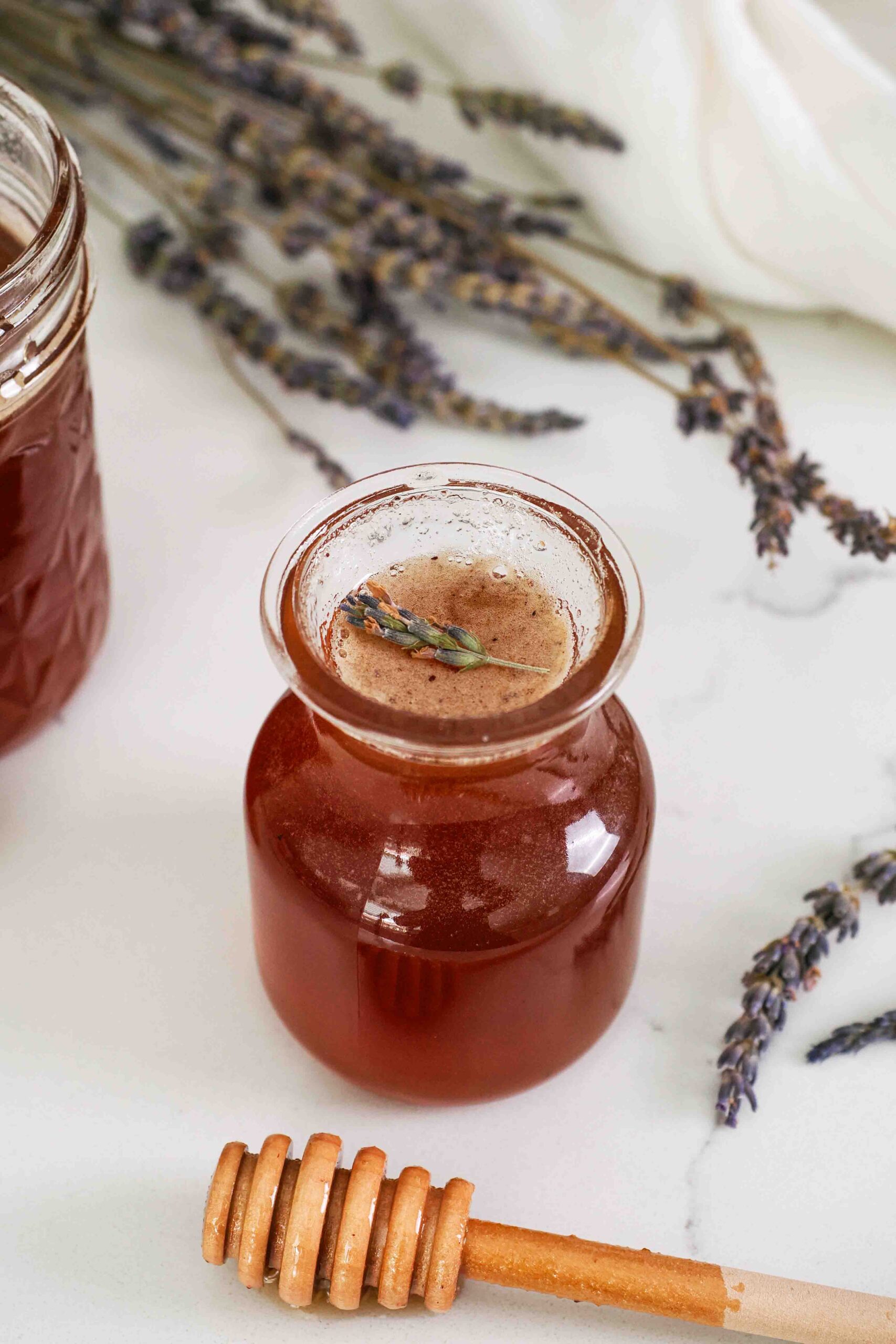 Closeup of a small bottle of honey lavender syrup with a honey dipper.