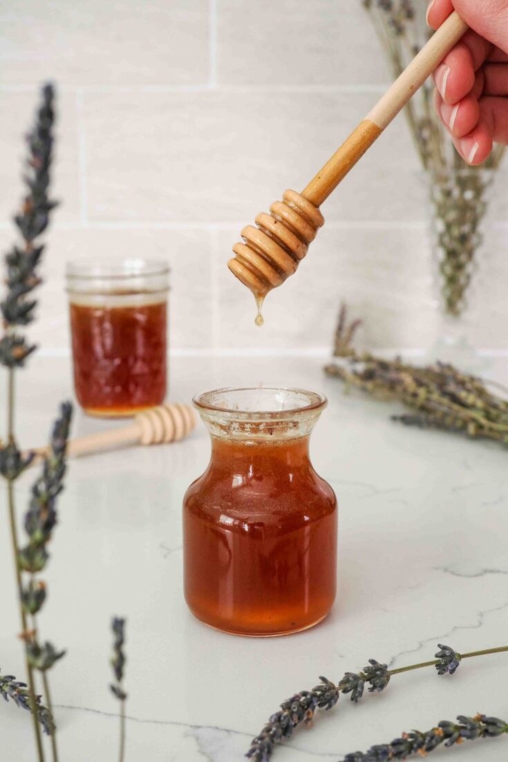 A wooden honey dipper drips honey lavender syrup into a small bottle.