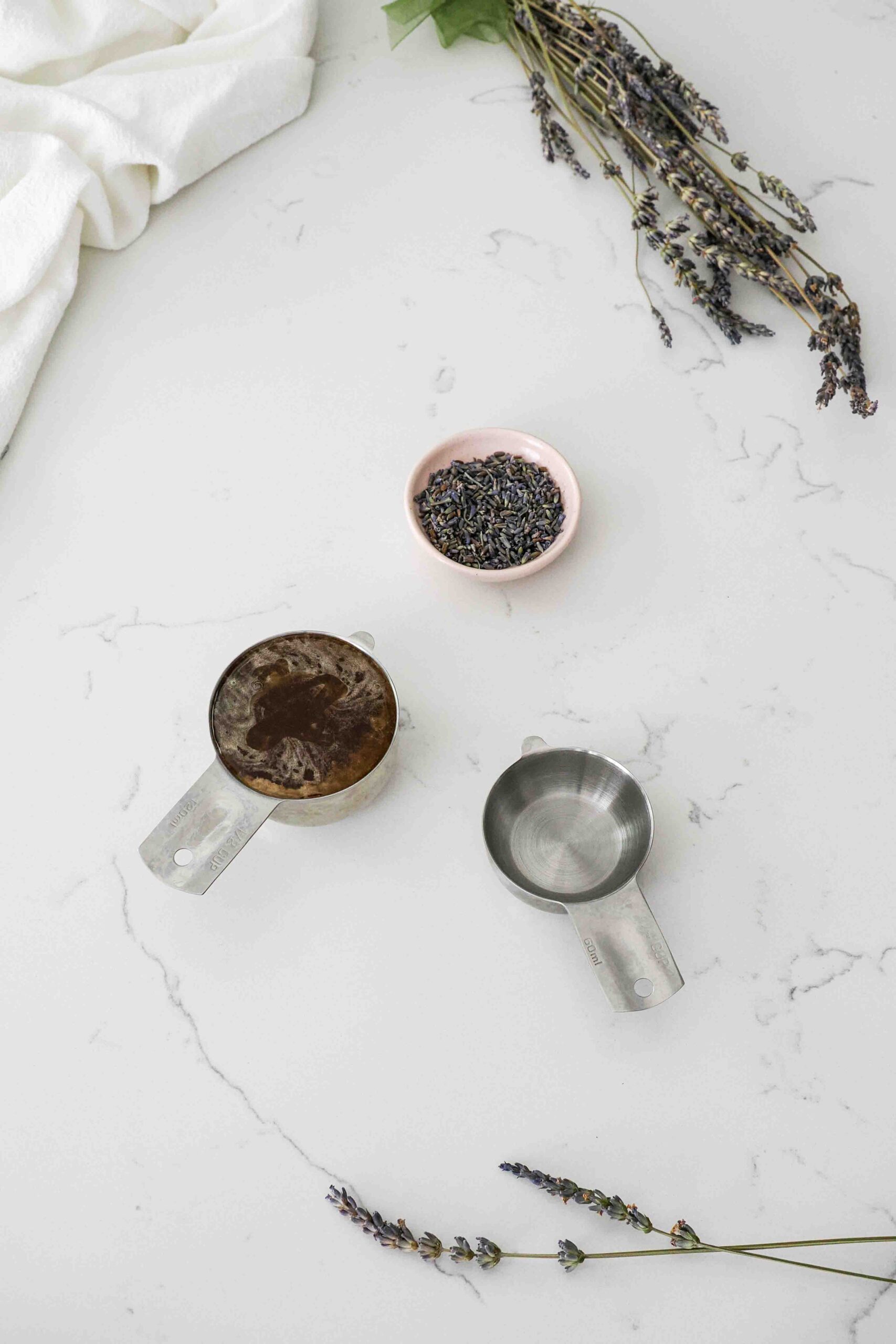 Honey, lavender, and water in measuring cups on a white countertop.