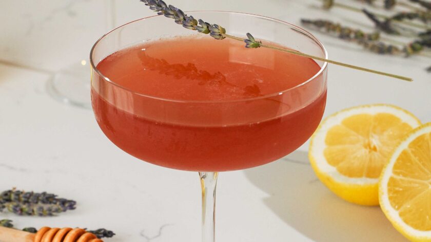 A dark pink cocktail in a coupe glass with a lavender sprig garnish.