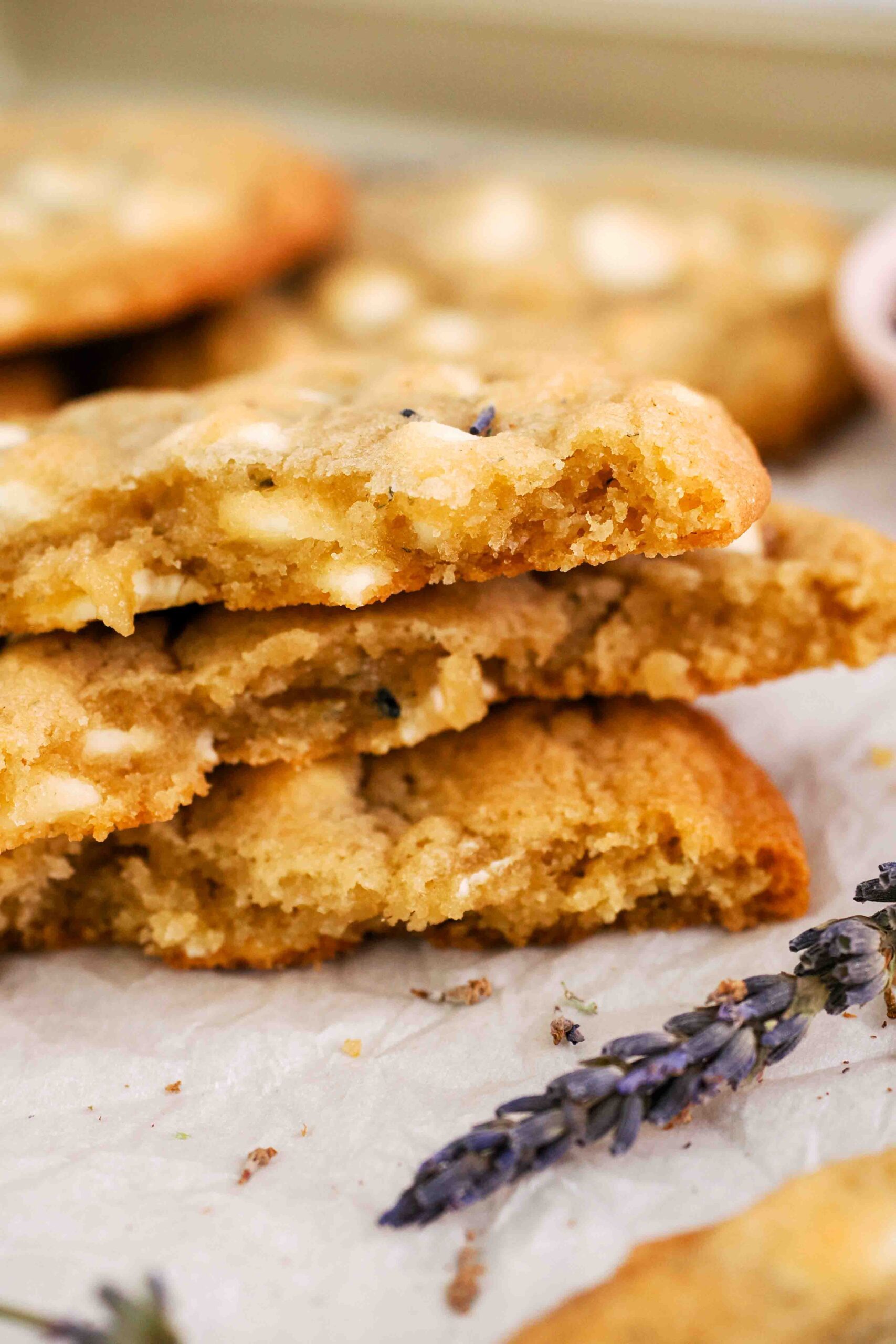 Lavender white chocolate chip cookies broken in half and stacked on parchment paper.