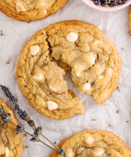An overhead view of a lavender chocolate chip cookie broken in half with lavender sprigs nearby.
