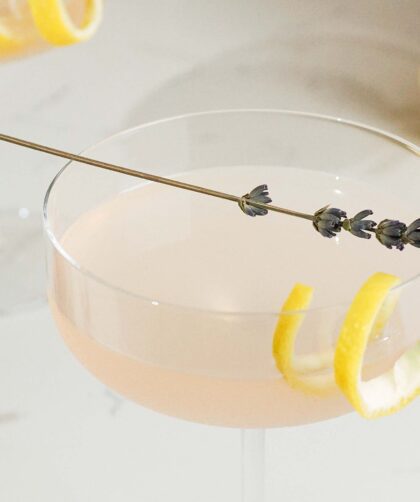 A closeup of a lavender lemon martini with a lavender sprig and lemon twist garnish.