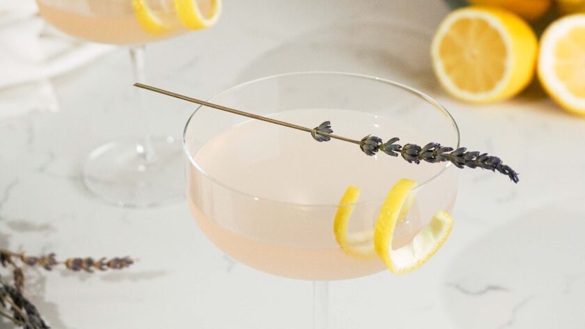 A closeup of a lavender lemon martini with a lavender sprig and lemon twist garnish.
