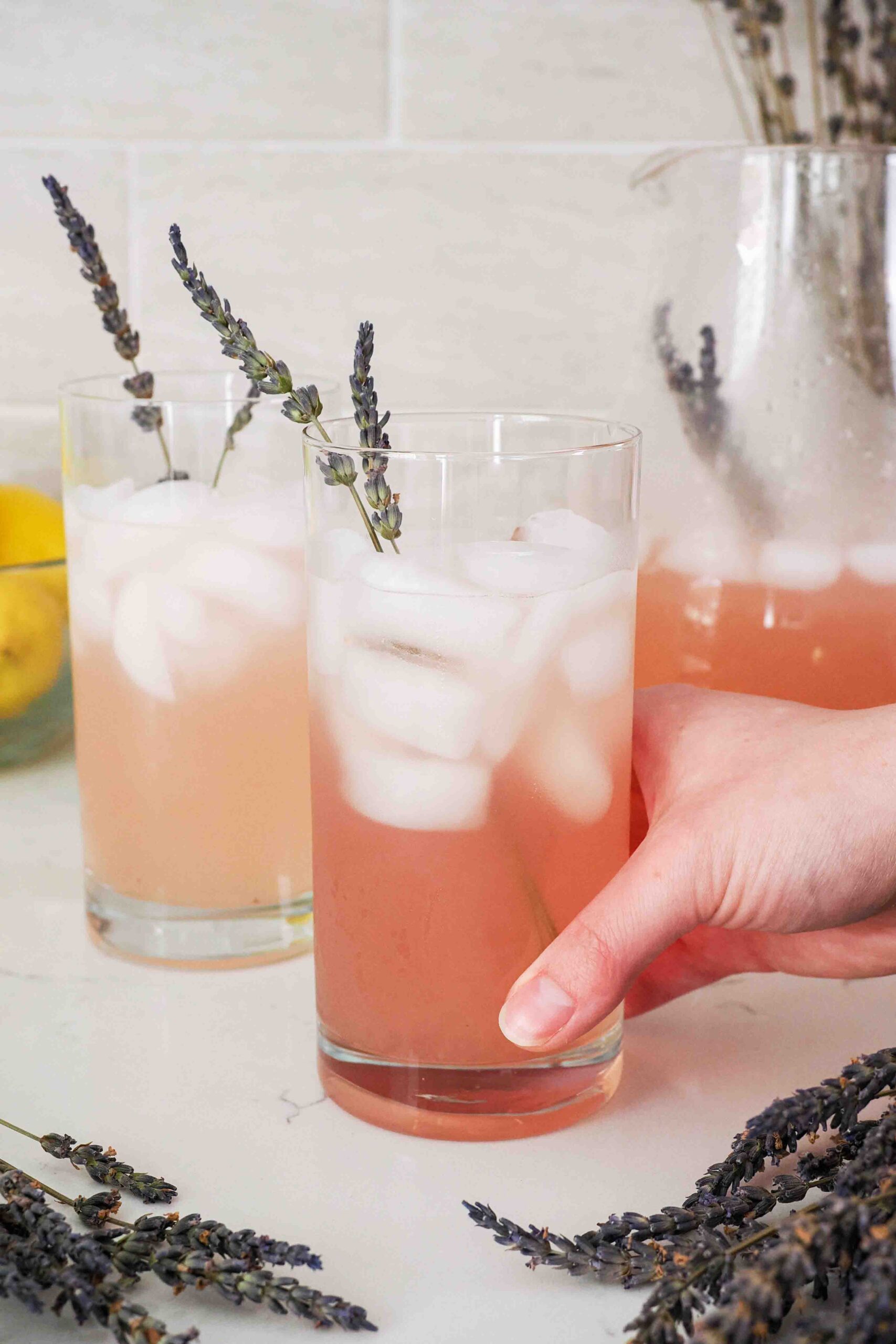 A hand holds a glass of lavender lemonade with lavender sprigs.