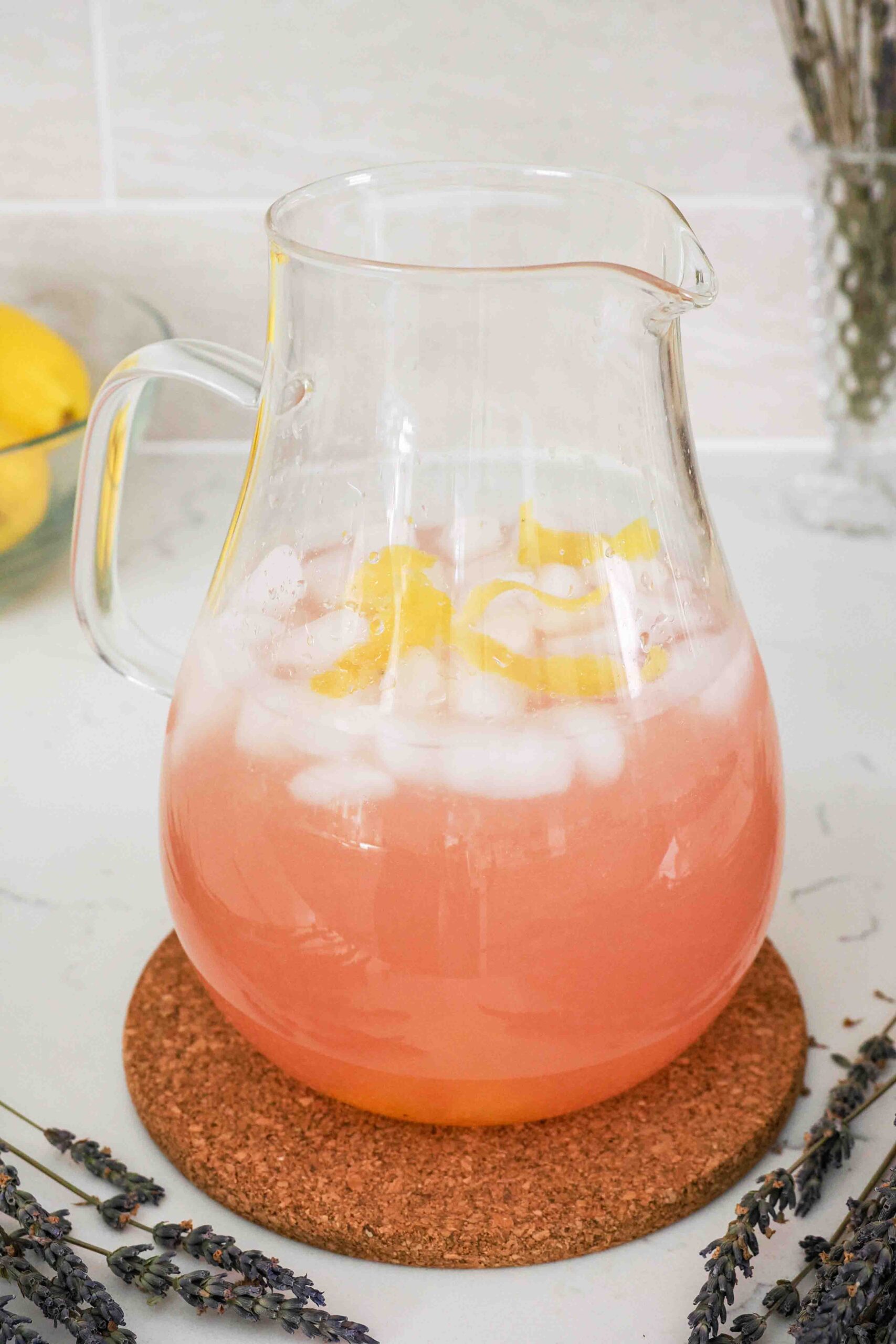 Lemon zest peels and ice cubes float in a pitcher of pink lavender lemonade.